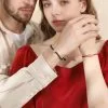 Pareja tomada de la mano luciendo pulseras de trébol de plata a juego.